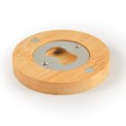 A round wooden wall-mounted bottle opener with a metal opening and two screws securing it.