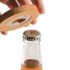 A wooden bottle opener above a capped glass bottle with brown liquid on a white surface.