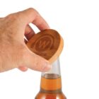 A hand places a wooden bottle cap with a stylized W logo onto a brown glass bottle.