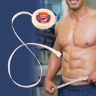 A muscular man measuring his waist with a Universal tape measure, with gym equipment.