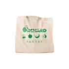 A beige tote bag with the words Orchard Pantry printed in green. Above the text are icons of various fruits including a cherry, apple, banana, orange, and a whole apple. The bag has two handles.