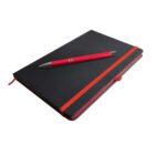 A closed black notebook with a red elastic band lies on a surface. A red pen with silver accents rests diagonally on top of the notebook. A red ribbon is visible at the edge of the notebook.