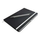 A closed black notebook with a white elastic band is placed on a white surface. A gray pen rests on top of the notebook.