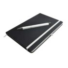 A closed black notebook with a white elastic band lies on a surface. A white and black pen is placed diagonally on top of the notebook. The notebooks ribbon bookmark is visible near the bottom left corner.