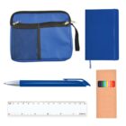 A collection of school supplies includes a blue pouch with zippers, a blue notebook, a blue pen, a set of colored pencils in a brown box, and a white ruler with measurements in centimeters.