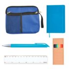 A flat lay image featuring a blue zippered pouch with a mesh pocket, a blue notebook with an elastic band, a set of colorful pencils in a cardboard box, a blue pen, and a transparent 15 cm ruler with measurements.