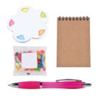 Assorted stationery items: a notepad with spiral binding, a pink pen, a flower-shaped sticky note pad with colorful edges, and a small packet of multicolored jelly beans.