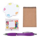 A notepad, sticky notes shaped like a painters palette, a packet of colorful jelly beans, and a purple pen with silver accents are arranged on a white background.