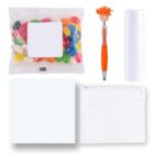 A collection of items including a pack of colorful jelly beans, an orange pen with a smiley face topper, a white lip balm tube, a white cleaning cloth, and a transparent zippered pouch.