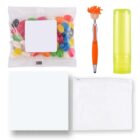 A collection of items including a packet of colorful jelly beans, an orange pen with a smiley face topper, a green translucent tube, and two white squares—one cloth and one zippered pouch.