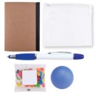 A flat lay of various items: a brown notebook with a black spine, a white zippered pouch, a blue and white pen, a small packet of colorful jellybeans, and a blue stress ball.