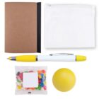A flat lay image of desk items: a brown notebook, a white zip pouch, a white and yellow pen, a packet of colorful jelly beans, and a yellow stress ball.