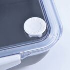 Close-up of a transparent container lid with a white circular vent that reads PULL TO RELEASE. The lid shows a secure closure, with part of the container visible beneath it.