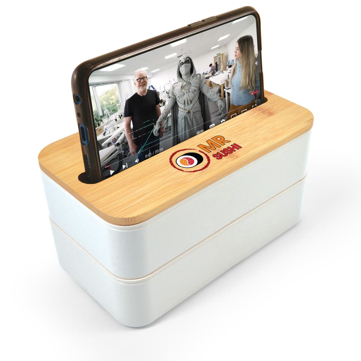 A smartphone is placed on a light wooden box with a video playing, showing three people. The box has the logo MR gadget on it. The setup suggests an amplified sound system for the phone.