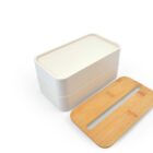 A white rectangular lunchbox with two stackable layers is shown on a white background. The lid, placed beside it, is wooden with a long slot for easy opening.