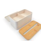 A two-tiered beige bento box with a bamboo lid and a plastic lid. The top tier has a divider, and both tiers are rectangular. The bento box is open, displaying its interior design on a white background.