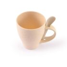 A beige mug with a textured speckled pattern, featuring an integrated handle and spoon slot. A matching spoon is securely attached at the top of the handle. The mug is empty and placed against a white background.