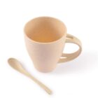 A beige, speckled mug with a sturdy handle is placed beside a matching spoon on a white background. The mug has a simple, rounded design, and the spoon is slightly curved.