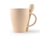 A beige, speckled ceramic mug with a matching spoon rests in its handle. The mug has a smooth, slightly tapered shape and the spoon is rounded at the top. Both items have a minimalist design and are set against a plain white background.