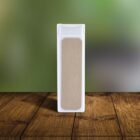 A rectangular white foot file with a sandpaper-like surface stands upright on a wooden surface with a blurred green background.