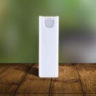 A tall, white rectangular spray bottle with a round button on top stands on a wooden surface against a blurred green background.