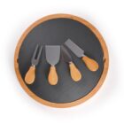 A round cheese board with a black slate center and wooden rim. On it are four cheese knives, each with a wooden handle, arranged neatly. The knives are different shapes for various cheese types.