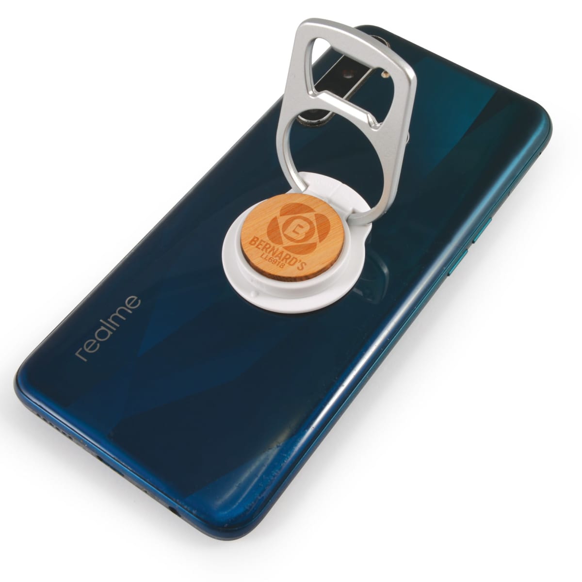 A smartphone with a dark blue back is shown with a pop-out stand attached featuring a bottle opener. The stand has a wooden accent with an engraved logo. The phone has a dual camera setup and the brand realme is visible.