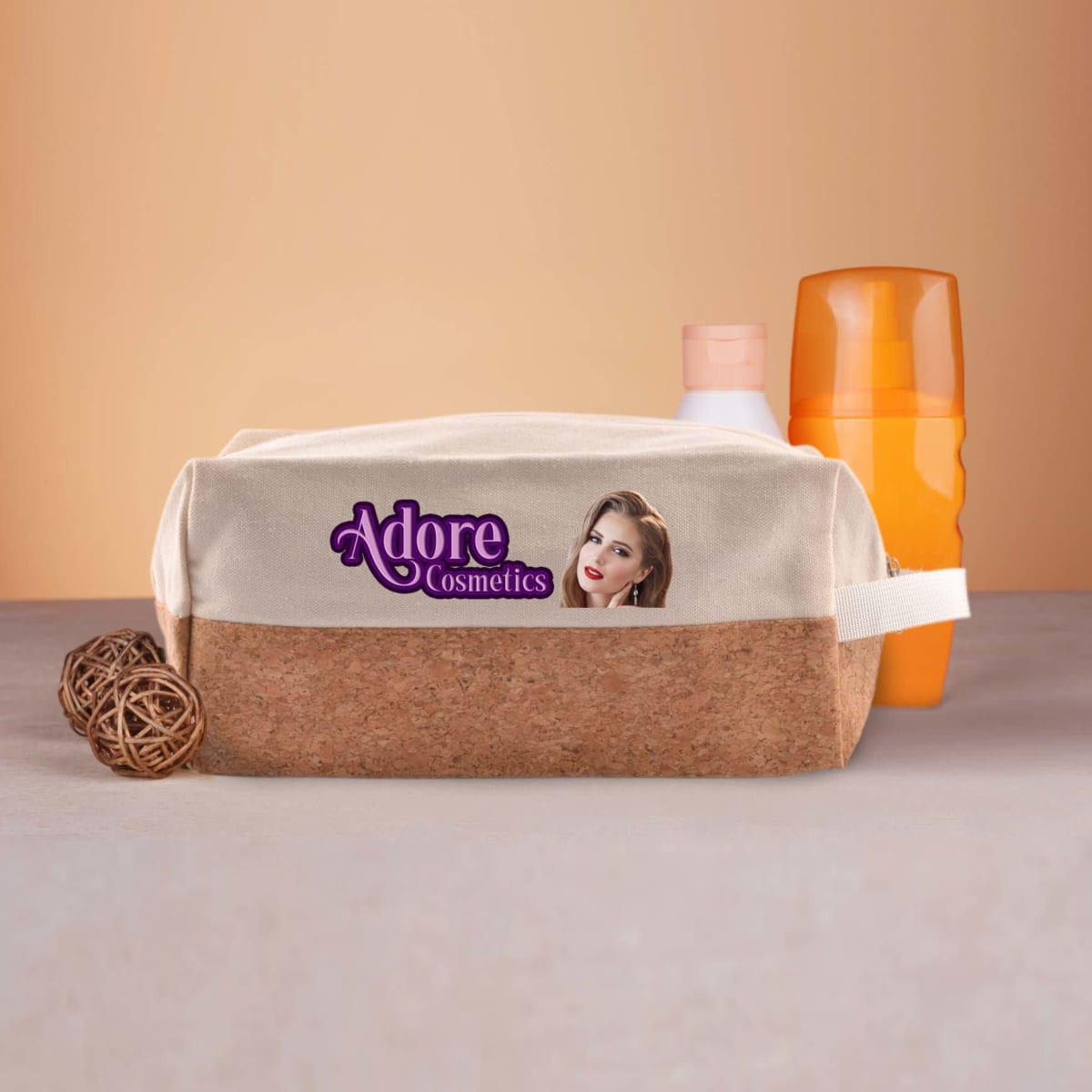 A cosmetics pouch labeled Adore Cosmetics with an image of a woman on the front. It is placed on a surface with a wicker ball and two orange and white bottles in the background.