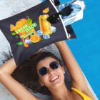 A woman in sunglasses lies by a pool, smiling. She holds a large bag with a cartoon orange, reading Fresh Juice 100% Natural, and a can of orange drink and ice cubes illustrated. A rolled towel and sunglasses are visible in the bag.