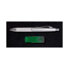 A silver pen with a textured grip and a clip is placed above a green and black swivel USB flash drive on a black textured surface.