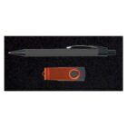 A ballpoint pen with a black barrel is placed above an orange USB flash drive on a black textured surface.