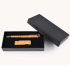 A bamboo pen and USB flash drive in an open black gift box. The pen has silver accents, and the USB drive matches the pen’s bamboo material. The top of the box is placed beside the open box.