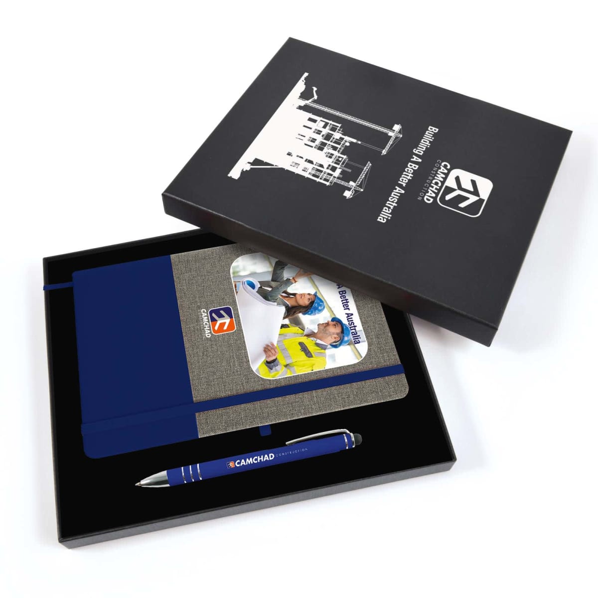 An open black box displays a gray notebook with a construction-themed cover inside, featuring workers wearing hard hats. Below the notebook is a blue pen labeled CAMCHAD. The box lid features a white building graphic and the text Building the Future.