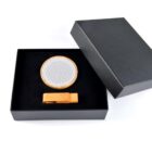 A black gift box containing a round item with a wooden rim and a mesh surface, alongside a small wooden clip. The box lid is partially open and black. The items are neatly arranged on a white background.