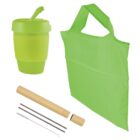 A green reusable coffee cup, a matching green reusable shopping bag, a bamboo straw case, two metal straws, a cleaning brush, and a straw cleaner are displayed against a white background.