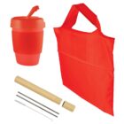 Red reusable coffee cup with lid, red foldable shopping bag, metal straw with cleaning brush, and a beige case with caps for the straw. Eco-friendly set displayed on a white background.