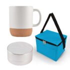 A white ceramic mug with a cork base, a silver portable speaker, and a blue insulated lunch bag with a black handle and zipper.