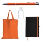 Collection of items including an orange pen, a bottle of hand sanitizer, an orange tote bag, and a black notebook with an orange ribbon. The items are arranged on a white background.