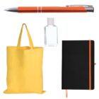 A flat lay image featuring an orange pen, a small bottle of hand sanitizer, a yellow tote bag, and a black notebook with an orange elastic band and a matching ribbon bookmark.