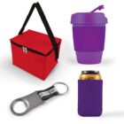 A collection of promo items: a red insulated lunch bag with black straps, a purple reusable coffee cup with a lid, a metal bottle opener with a black handle, and a purple can cooler with a soda can inside.