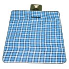 A blue and white plaid picnic blanket with green edges is laid flat. At the top, theres a folded green section with a handle, indicating that it can be rolled up and carried easily.