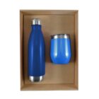 A blue insulated bottle and a blue insulated cup with silver lids are placed side by side in a brown cardboard box. The bottle is taller and cylindrical, while the cup is shorter and rounded.
