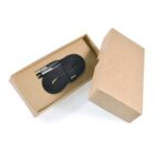 A black USB-C charging cable is neatly coiled and secured with a strap, resting inside an open brown cardboard box. The lid of the box is positioned on its side to the right. The packaging is simple and eco-friendly.