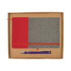 A red and gray fabric-covered notebook sits in a brown box alongside a purple and silver pen, with a red elastic band securing the notebook closed.