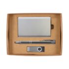 A gift set in a cardboard box containing a silver business card holder, a silver pen, and a silver USB flash drive. The items are neatly arranged in compartments within the box.