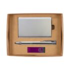 A cardboard gift box containing a silver business card holder, a sleek silver pen, and a purple USB flash drive. The items are neatly arranged against a simple brown background.