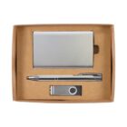 A brown box containing a silver business card holder, a silver pen, and a silver USB flash drive. The items are neatly arranged with the pen in the center, surrounded by the card holder above and the USB drive below.