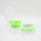 Two small green containers are on a white background. One is open, showing a rolled silicone item inside. The other is closed, with a cartoon grandmas face and the words Nanas Kitchen on the lid.