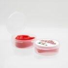 Two small, round, clear plastic containers with lids. One is open, showing red silicone earplugs. The other is closed, with a colorful cartoon dog design and text on the lid.