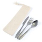 A beige cloth pouch next to three stainless steel utensils: a knife, a fork, and a spoon. The pouch has a drawstring at the top. The utensils are neatly arranged and have a reflective surface.